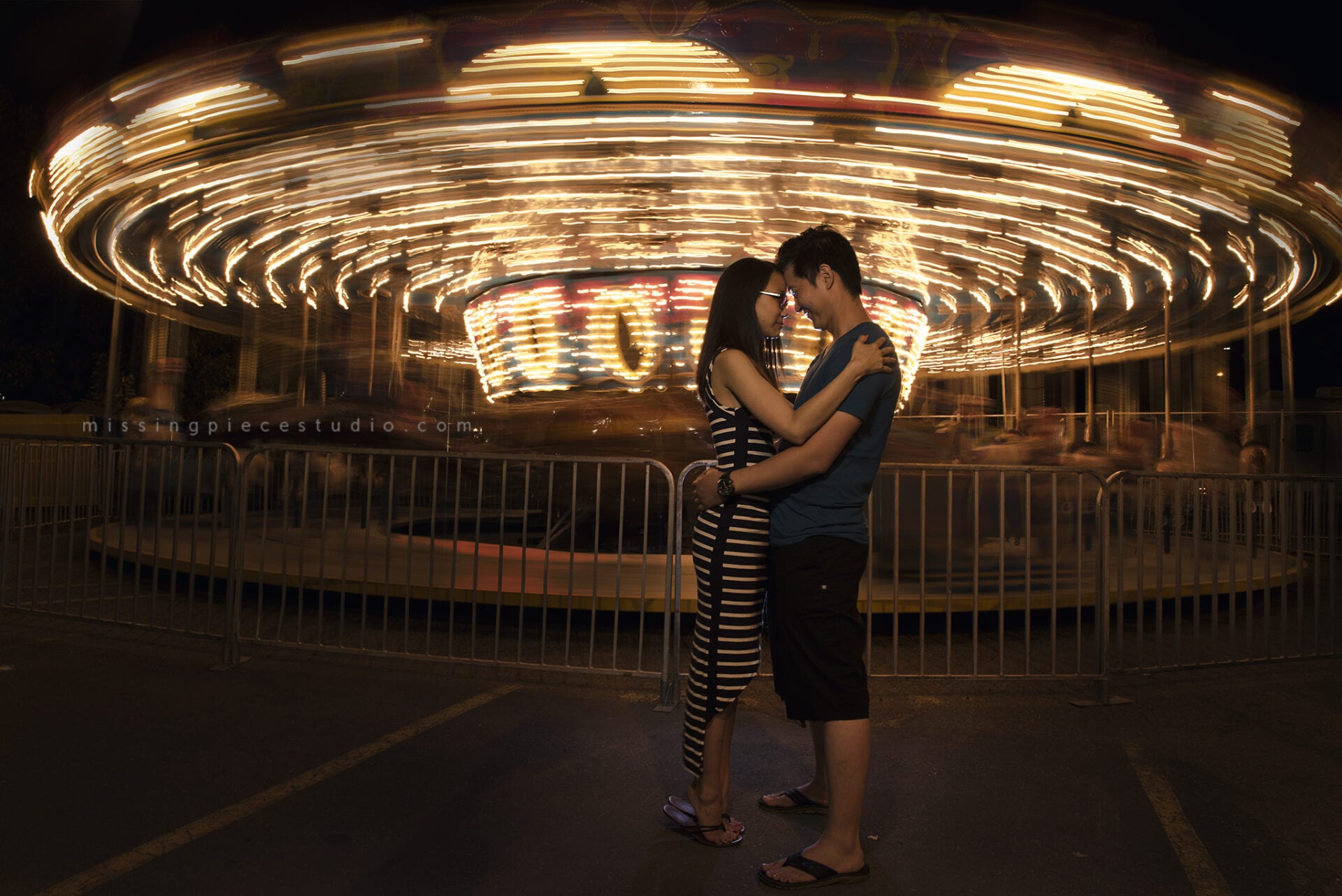 A couple posed in front of a spinning merry go round carousel
