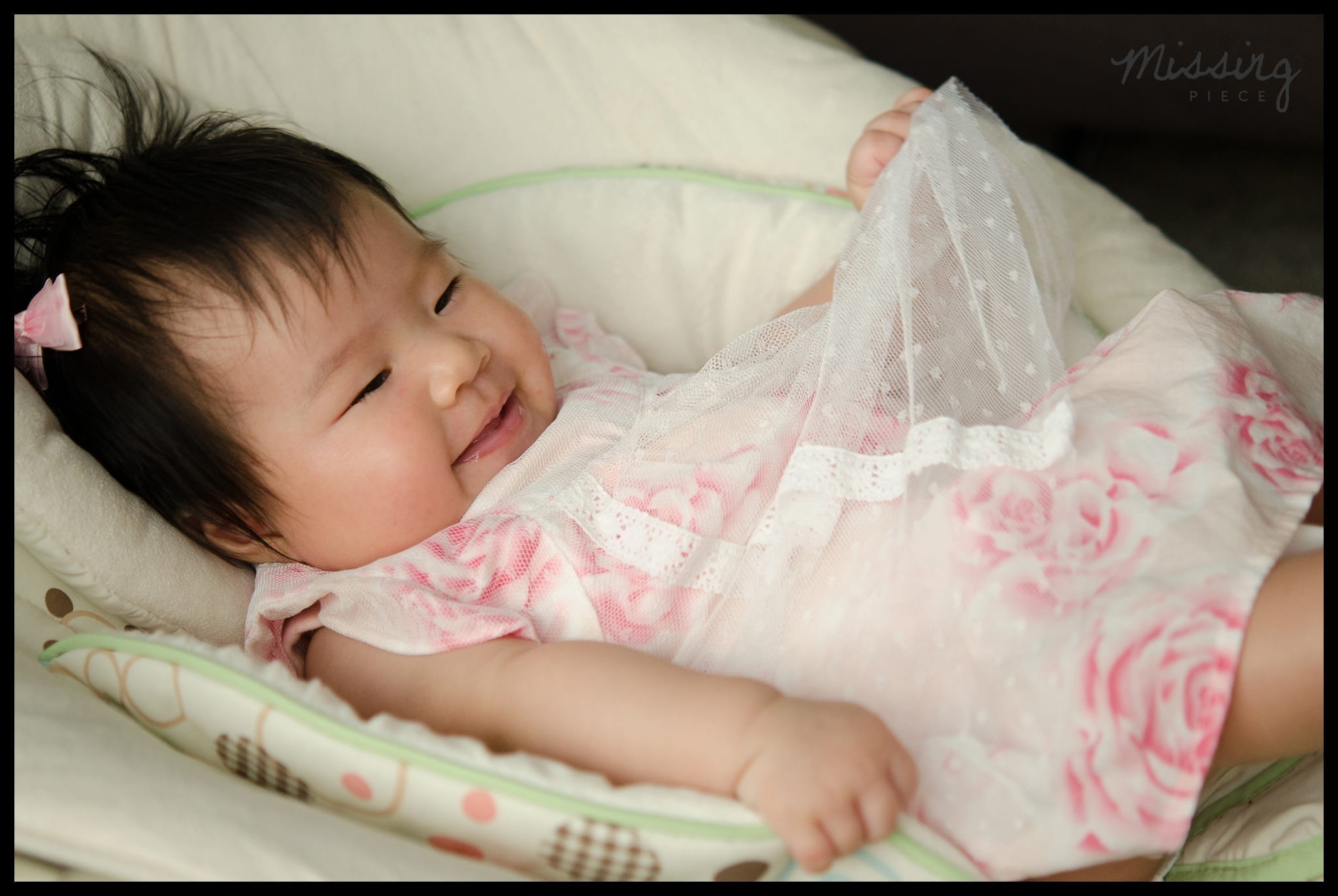 A cute baby girl smiles as she plays with her dress while laying on her crib