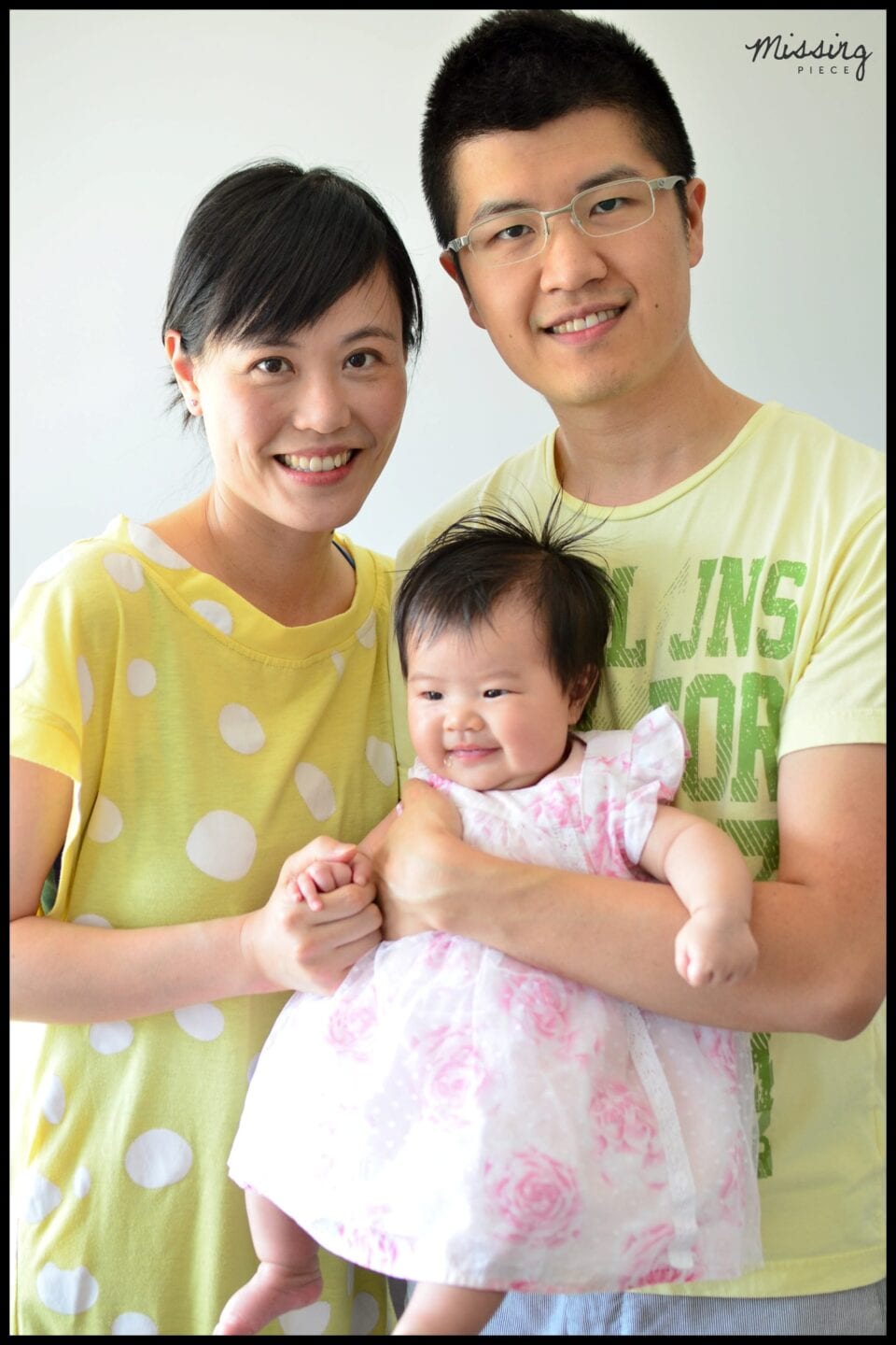 Mother and father smiles for a picture with their baby in their hands
